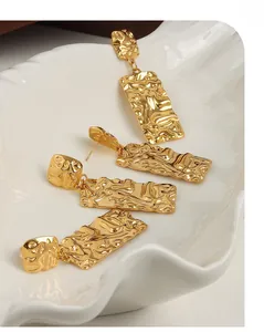Close-up of golden titanium earrings with irregular pleated texture on white tray