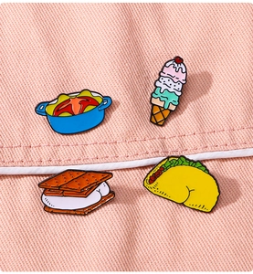 Detailed view of four colorful enamel pins including ice cream and taco on pink denim fabric