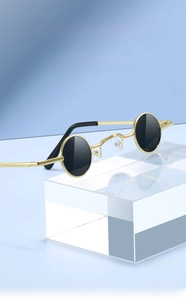 Detail of round punk sunglasses with gold metal frame and dark lenses on acrylic stand