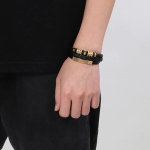 Détail d'un bracelet multicouche en cuir tressé noir avec accents métalliques dorés au poignet