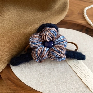 Détail macro de la pince à cheveux fleur tissée avec un bijou en forme de cœur bleu