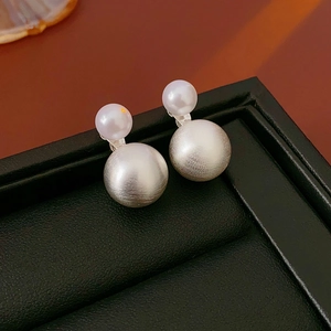 Macro detail of silver brushed metal ball and white pearl on a double-sided earring