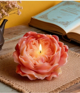 Close-up of a lit pink-orange gradient Austin rose candle with multilayered petals