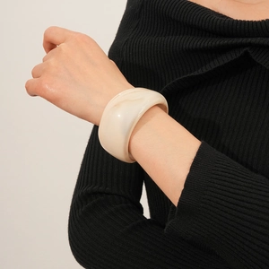Macro detail of creamy white marble resin wide bangle on model wearing black knitwear