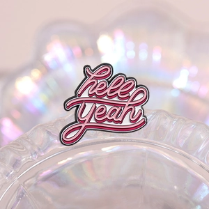 Pink and white enamel pin with Hell Yeah slogan on iridescent glass container