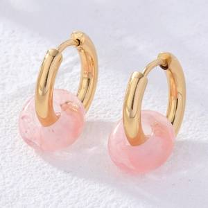 Detail of gold hoop earrings with doughnut-shaped pink natural stone pendants