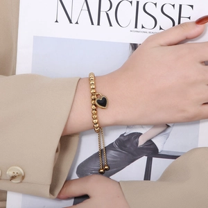 Bracelet en perles d'acier inoxydable doré avec pendentif cœur noir au poignet du mannequin