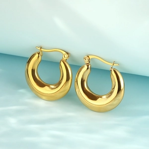 Polished gold thick oval hoop earrings on light blue water reflection background
