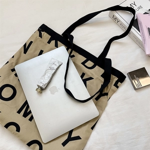 Flat lay of khaki canvas tote bag with letter print and black shoulder straps