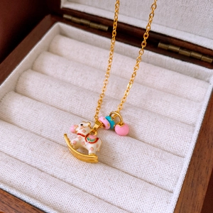 Detail shot of golden rocking horse pendant with colorful enamel and heart charm in a box