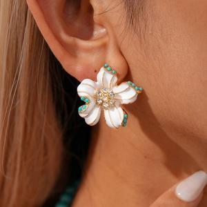 Close-up of elegant flower stud earrings with white enamel petals and turquoise beads