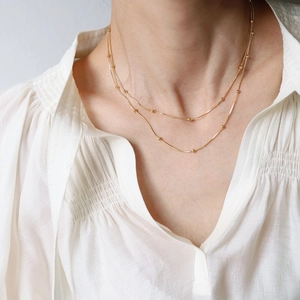 Double-layered gold snake chain necklace with small beads worn by a model