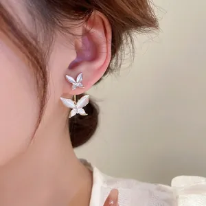 Elegant gold double butterfly stud earrings with pearlescent wings on a model's ear