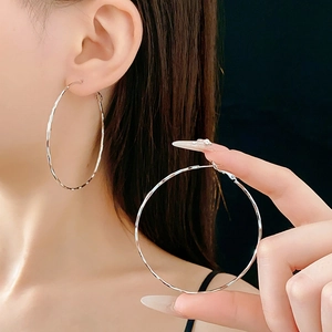 Dettaglio di grandi orecchini a cerchio argento geometrici con finitura a onde su modella