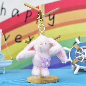 Close-up of cute pink plush bunny keychain with purple flower detail on wooden stand