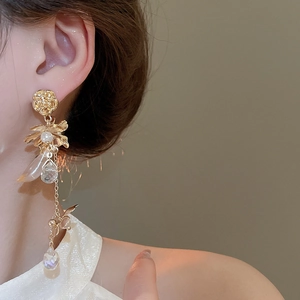 Close-up of long gold flower pearl tassel earrings worn by a model in warm light