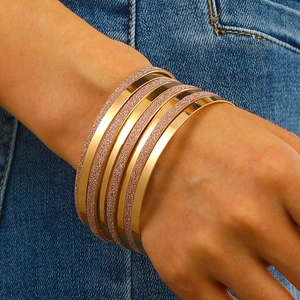 Macro view of gold stacked bangles featuring alternating polished and frosted textures