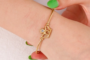Detailed close-up of a golden crown bangle with a centered crystal on a woman wrist