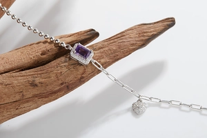 Close-up of S925 silver bracelet with purple gemstone and heart charm on driftwood