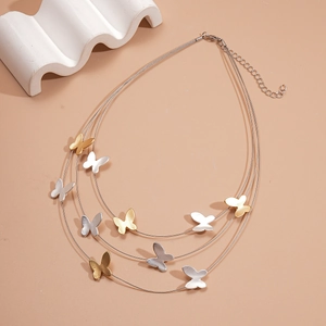 Detail of multi-layer butterfly necklace with matte gold and silver pendants on pink surface