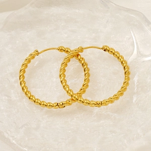 Macro detail of 18K gold twisted rope hoop earrings on transparent glass tray