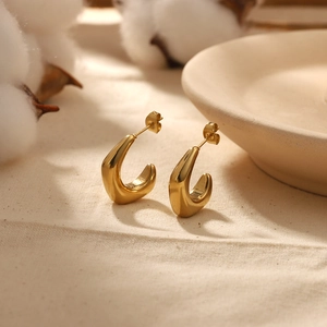 Polished 18K gold plated stainless steel C-shape stud earrings on beige fabric background
