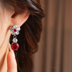 Detail of flower earrings with red zircon stones on model in warm lighting