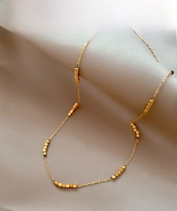 Close-up of a gold-plated beaded necklace with tiny cube charms on draped fabric