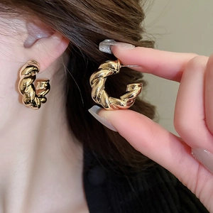 Close-up of golden croissant-style C-shaped earrings with a twisted metallic texture