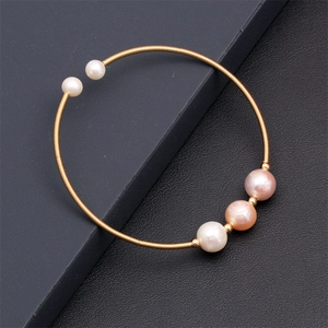 Detail of gold coil bracelet with five mixed-color freshwater pearls on textured background