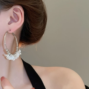 Detail view of large silver hoop earrings with white acrylic flowers on a model