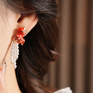 Close-up of vintage gold earrings with red enamel dragon and white pearl tassels
