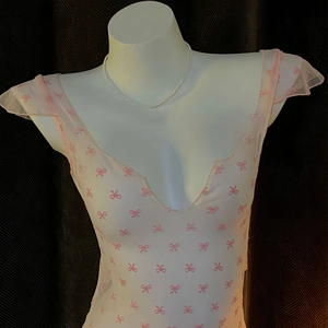 Pink bow print sheer mesh top with deep V-neckline and ruffled cap sleeves on a mannequin