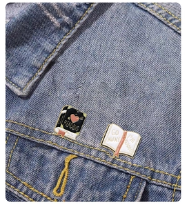 Detail of book-shaped enamel pins reading I LOVE READING and GO AWAY on denim jacket