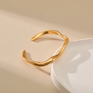 Detalle de brazalete dorado ondulado irregular con acabado espejo sobre plato blanco