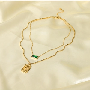 Close-up of golden layered necklace with green gemstone and sun-moon engraved pendant