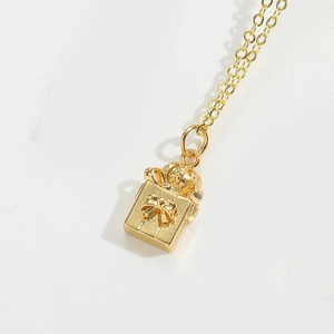 Close-up of gold gift box pendant with bow detail on a delicate necklace chain