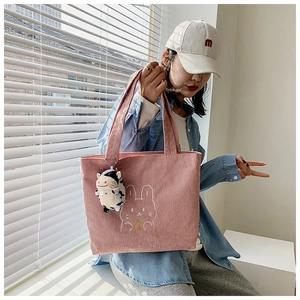 Detail of pink corduroy tote bag with rabbit embroidery and cute cow plush pendant