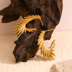 Detail of 18K gold plated wing earrings with radial feather texture on wood