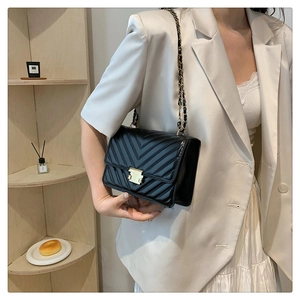 Detailed view of black quilted leather shoulder bag with gold chain strap worn by model