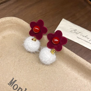 Macro shot of red flocked flower and white fur ball earrings on a beige tray