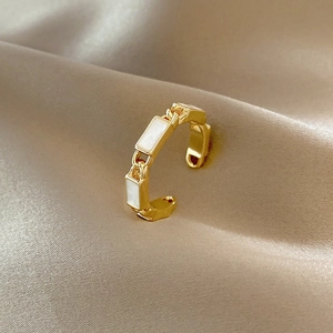 Macro shot of gold plated open ring with white enamel rectangular links on silk