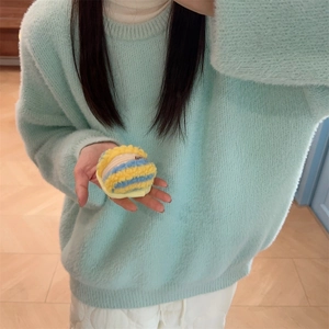 Close-up of yellow and blue striped plush pouch held by model in mint green sweater