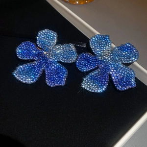 Detail view of five-petal flower earrings with blue gradient crystals on black velvet