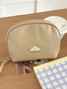 Close-up of beige semi-circle cosmetic bag with a gold house-shaped metal logo on wood table