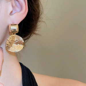 Close-up of golden metal earrings with geometric square and hammered round pendant texture