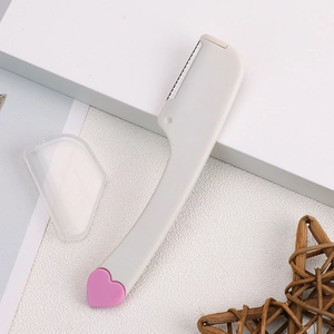 Compact white folding eyebrow razor with pink heart detail and clear safety cap