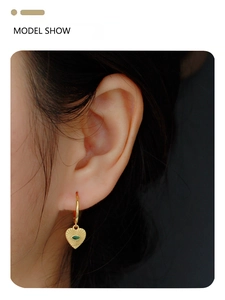 Detail of gold heart earrings with evil eye motif and green gemstone on female model