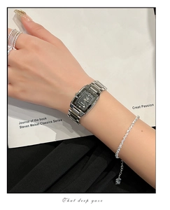 Detail of silver rectangular quartz watch with black dial and metal strap on woman's wrist