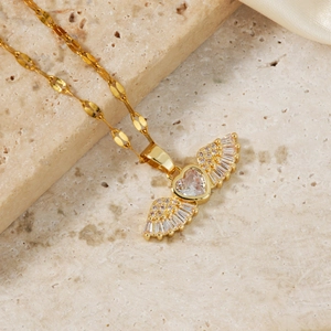 Elegant gold wing heart pendant necklace with clear zircon stones on a chic beige stone surface